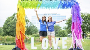 Two young adults smiling under rainbow arch at outdoor market4