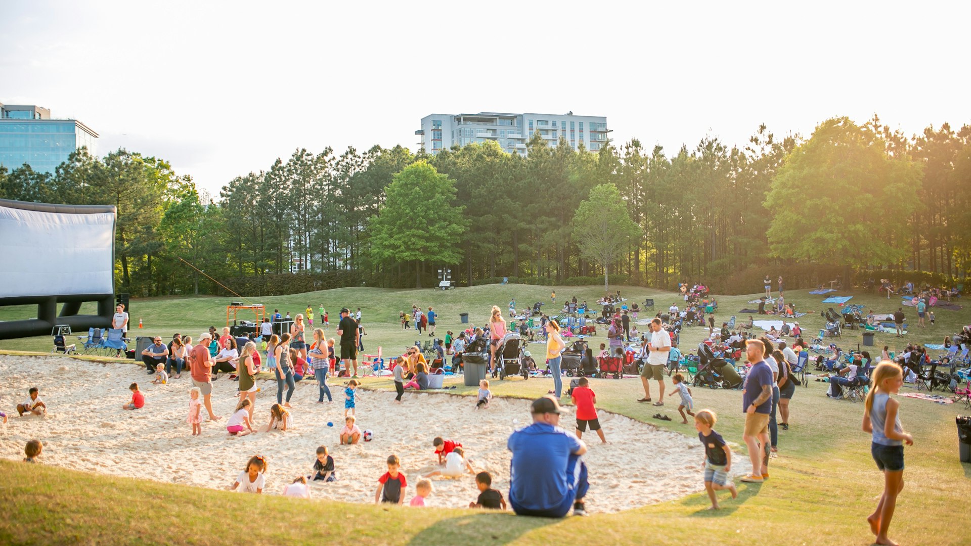 People in outdoor park near large movie screen at sunset