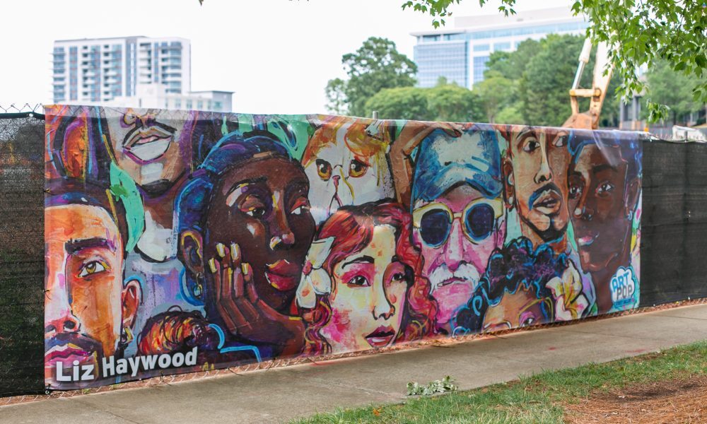 Construction fence in Ballantyne with printed art banner of faces by Liz Haywood from ArtPop Street Gallery5