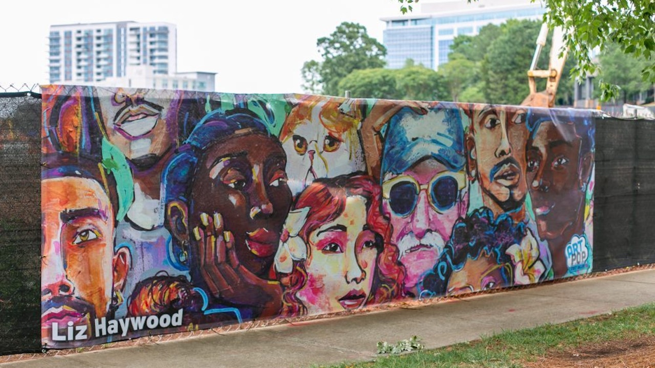 Construction fence in Ballantyne with printed art banner of faces by Liz Haywood from ArtPop Street Gallery5