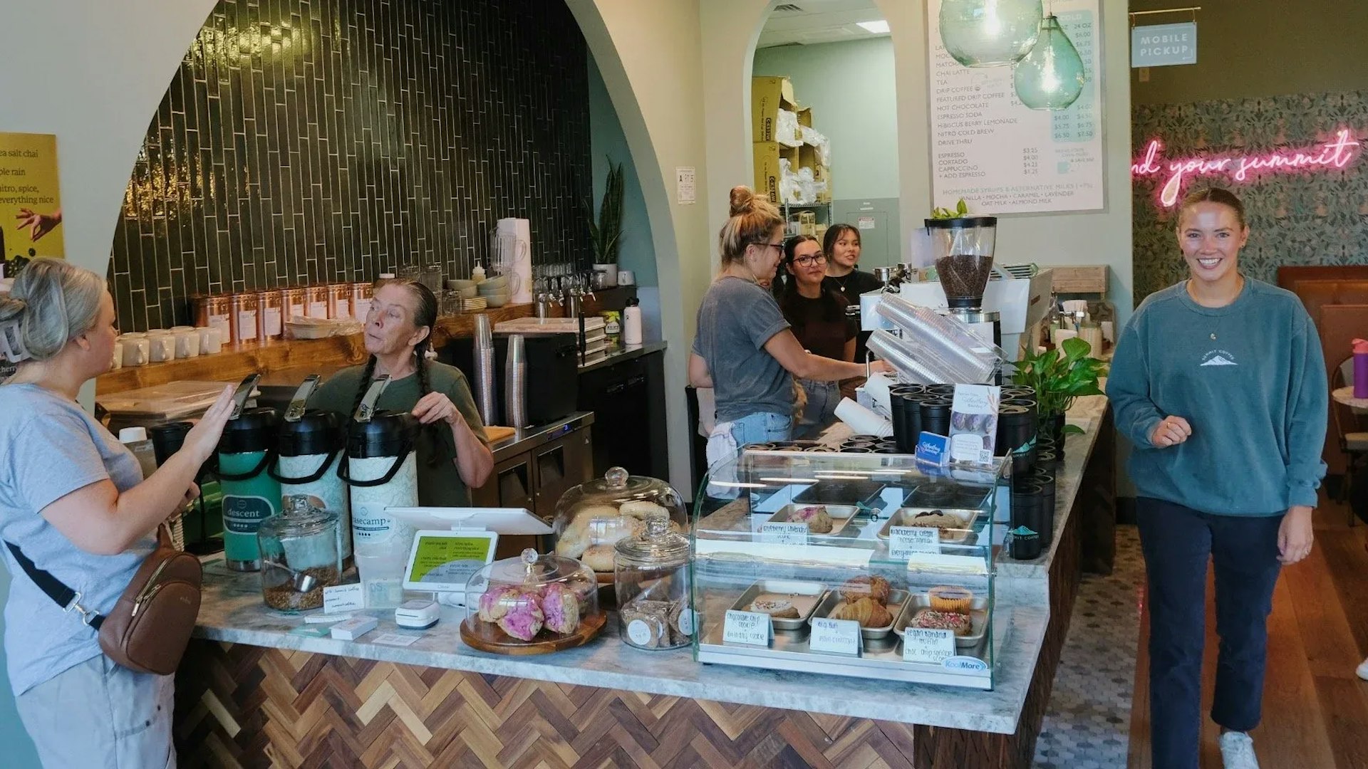 Summitcoffee Ballantynecafewithcustomerorderingatcounterwalkingaroundandsittingatbooths findyoursummit pinkneonsinkinthebackground